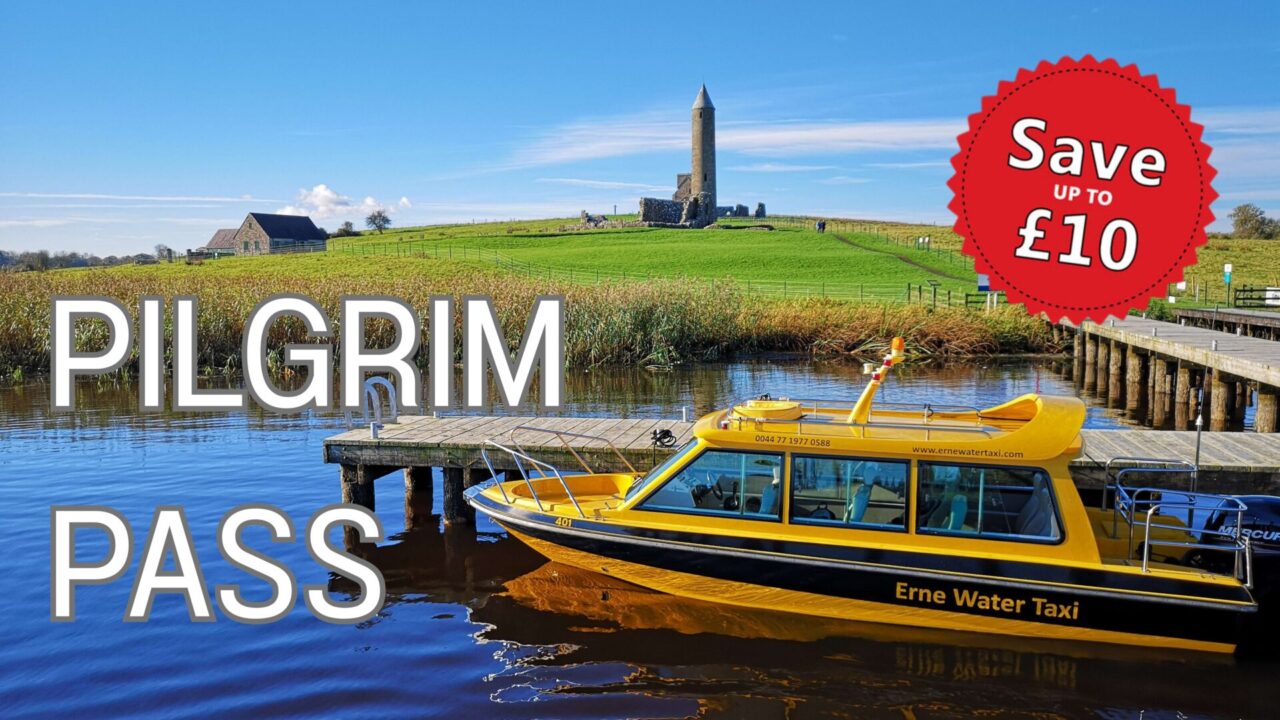 Erne Water Taxi's yellow boat moored at a jetty with Devenish Tower in the background